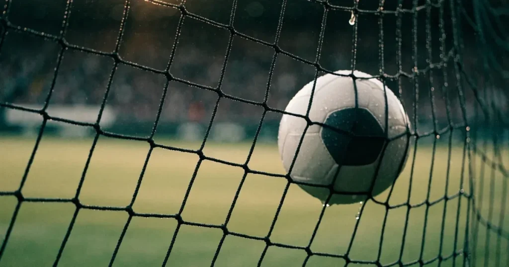 Ein Fussballnetz in Nahaufnahme, in dem ein Ball hängt, Wassertropfen glänzen auf den Maschen.